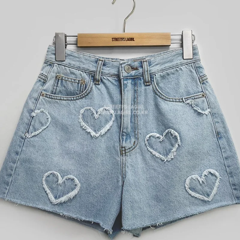 Shorts jeans de cintura alta com padrão de coração desfiado, cor clara e lavagem, perfeitos para looks leves e frescos no verão.