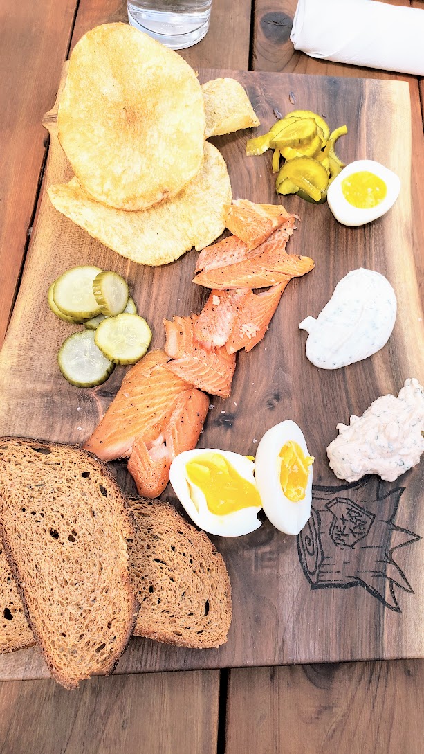 Tasty Lake Oswego Smoked Trout Board with cherrywood smoked trout, 8-minute egg, horseradish cream, onion dip, kettle chips, rye crostini, house pickles, and it is perfection with the assortment of salty, creamy, crunchy, sour, a little spicy, savory.