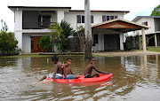 Children float on a board past houses surrounded by flood waters in the town of Ingham, located in North Queensland, Australia, March 11, 2018. 