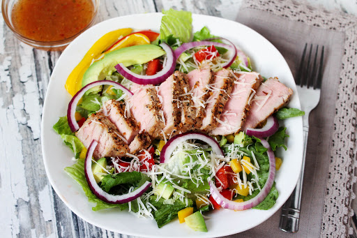 Tuna steak salad on a plate with dressing on the side.