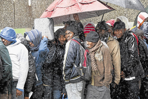 Men wait outside the Customs House building in Cape Town, hoping to get work permits so they can stay on in South Africa