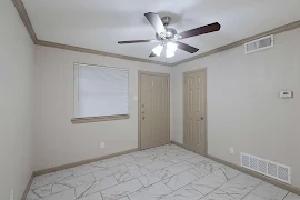 Vacant townhouse living room with beige walls, white tiled floor, ceiling fan, a window, and an entrance door.