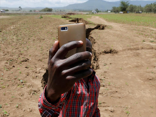 A man holds his phone to take a Facebook live video near a chasm suspected to have been caused by a heavy downpour along an underground fault-line near Mai Mahiu, March 28, 2018. /REUTERS