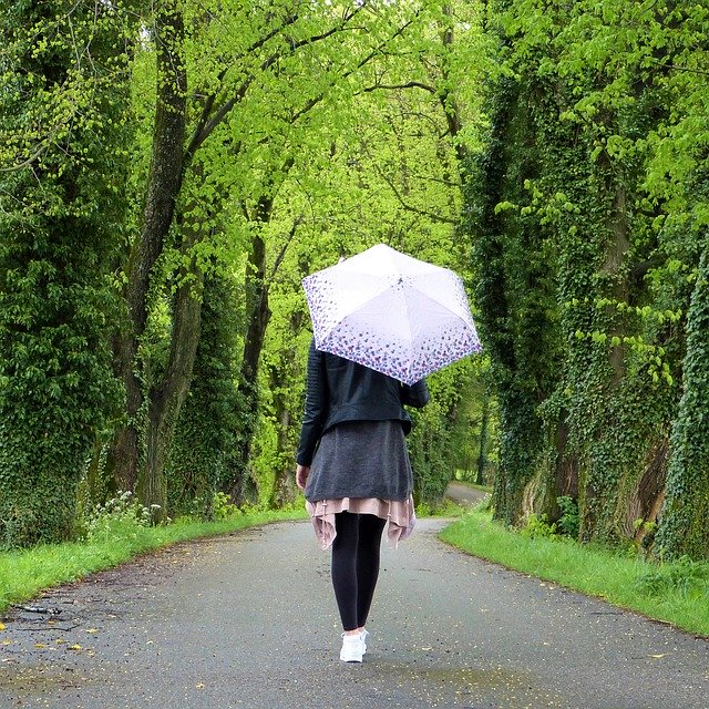 Frau mit aufgespannten Regenschirm beim Spaziergang im Wald