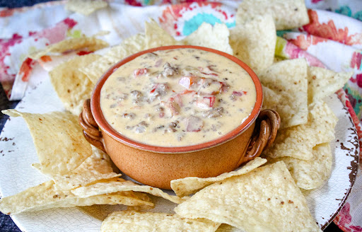 Bacon Cheeseburger Queso in a bowl with tortilla chips.
