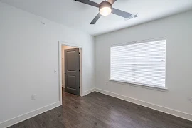 Bedroom with light walls and trim, wood-inspired flooring, window with blinds, ceiling fan, and a walk-in closet