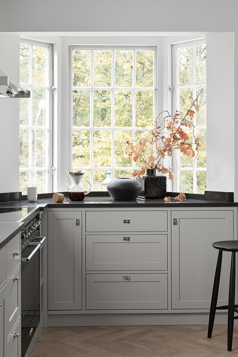 modern kitchen with white shaker cabinets and large paned window. black countertops provide contrast and a herringbone pattern wood floor adds a chic element to the design