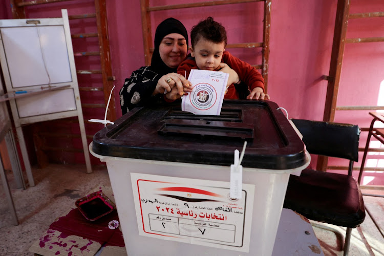 A woman casts a ballot with a child, at a polling station on the second day of the presidential election in Giza, Egypt, December 11, 2023.
