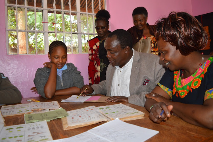 Jude Njomo Kiambu Mp (Seated) going through classwork of a pupil in the special needs programme in Kiambu primary school after the rehabilitation of the classrooms to modern status with teachers looking on