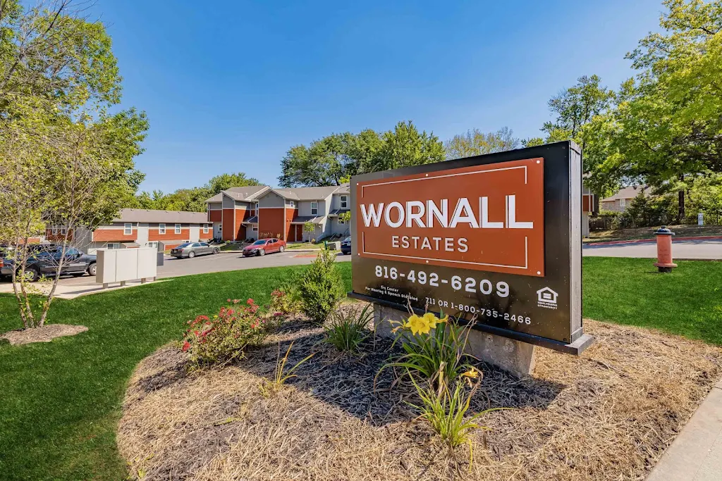 Wornall Estates community sign with plant and flower bed and view of parking lot and apartment building in the background