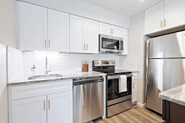 Modern apartment kitchen with white cabinets, stainless steel appliances, and subway tile backsplash.