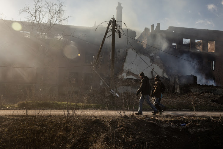 Residents walk past a smouldering building that was hit by recent Russian shelling on December 14, 2022 in Bakhmut, Ukraine. Russia continues its campaign to seize Bakhmut, Donetsk region, in what many analysts regard as an offensive with more symbolic value than operational importance for Russia.