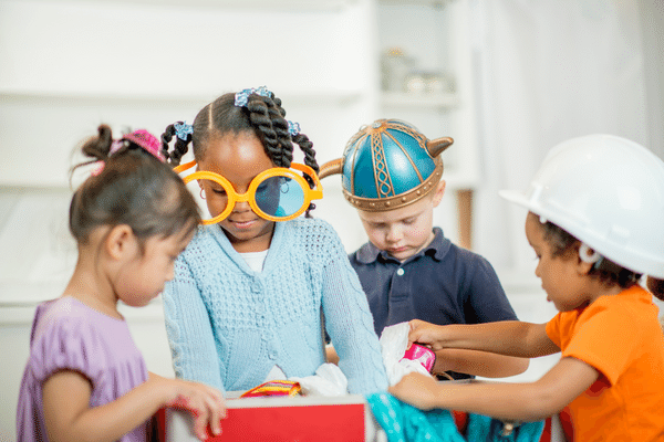 A multi-ethnic group of young children are playing dress up together and are wearing costumes.