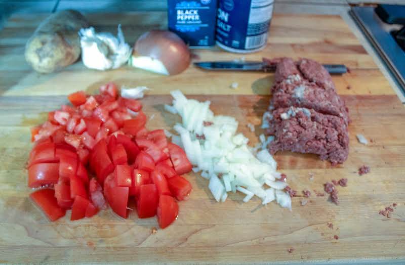 Onions, Tomatoes, And Corned Beef Chopped On A Cutting Board.