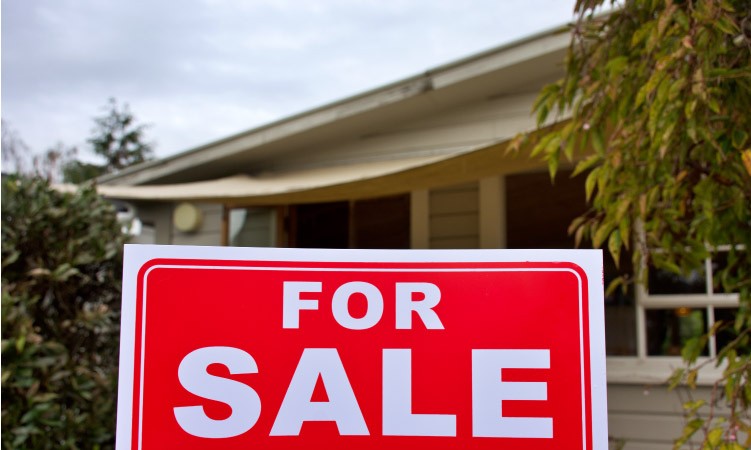 A fixer-upper house with a “FOR SALE” sign posted outside.