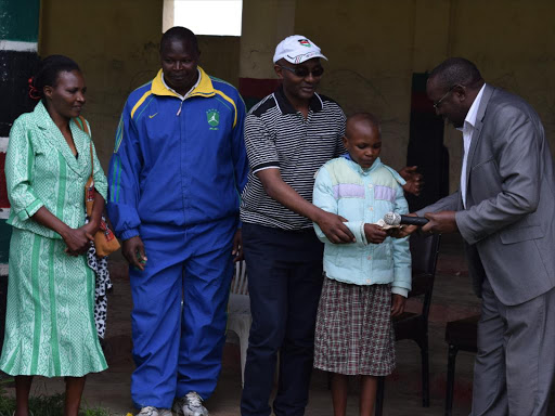 Athletics Kenya(AK)vice president in charge of youth development Barnabas Korrir,reward Lydia Njerir,12.Njeri was the youngest competitor in 5km race during the selection of Kipipiri Ndakaini Half marathon team.The event was held on Monday at Kipipiri stadium,Miharati.Looking on are Kipipiri mp,Samuel Gichigi,a Nyandarua athletics official,Wanyahoro and Njeri's mother.