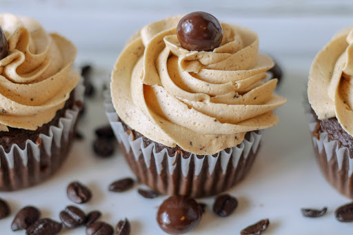 Easy coffee icing piped onto chocolate cupcakes with a chocolate covered coffee bean on top.