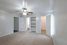 Bedroom with a walk-in closet, built-in shelves, and entry to a bathroom on the far wall and a wood-inspired ceiling fan.