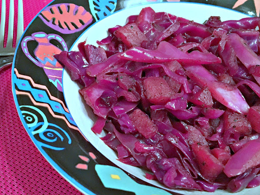 Red cabbage in a bowl sitting on a magenta table mat with a fork next to it.