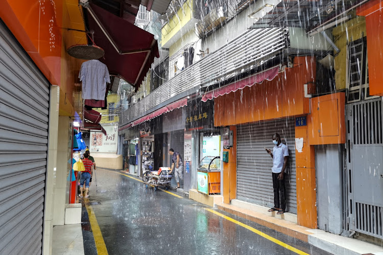 A man, wearing a face mask, shelters from the rain in Guangzhou’s Xiaobei neighborhood, nicknamed ‘little Africa’. Picture: REUTERS/DAVID KIRTON