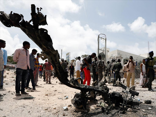 Somali security officers and civilians look at the wreckage of a vehicle destroyed at the scene where a speeding car exploded after it was shot at by police, outside the hotels near the presidential palace, in Mogadishu