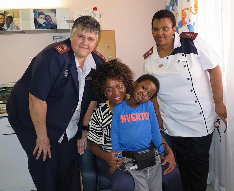 A happy, smiling Mnotho Mndebele safely in the arms of his mother, Mbali Mndebele, while showing off his heart ventricular assist device (HVAD). On hand to offer support is sister Ina Kok, acting deputy nursing manager (left) and Sr Bulelwa Ntilashe, a registered nurse.