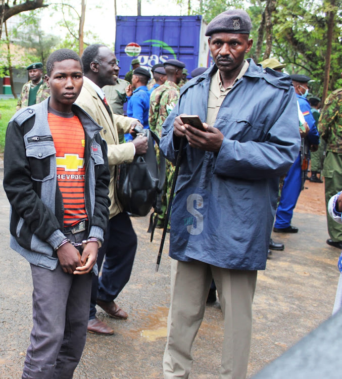 A handcuffed KCPE candidate Boniface Nguu at Museve Primary School in Kitui Central, is guarded by security at Kitui county commissioner’s office awaiting transport to his school to sit for the exam on November 28.