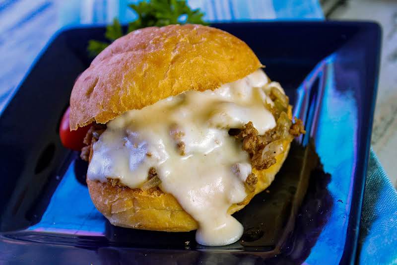 Philly Cheesesteak Sloppy Joe With Cheese Sauce Dripping Onto The Plate.