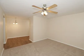 Living area with tan carpet and tan walls facing dining room