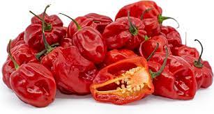 Pile of red lantern shaped peppers with one in the front cut in half revealing the membrane and seeds inside.
