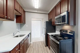 Kitchen with wood-inspired flooring, stainless steel appliances, wood cabinets, and white counters