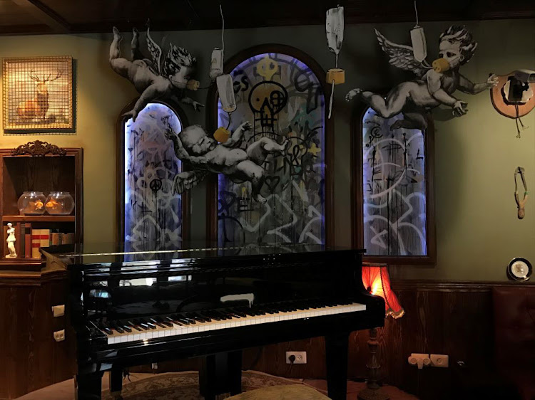 Three models of angels wearing oxygen masks hang from the ceiling above the piano in the dining room at the Walled-Off Hotel