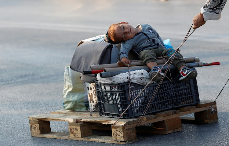 A woman pulls a baby on a pallet as they prepare to move to a new temporary camp on the island of Lesbos, Greece.