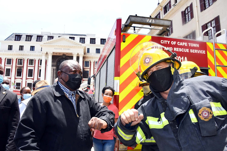 President Cyril Ramaphosa bumps elbows with a firefighter as he inspects damage after a fire broke out at the parliament buildings in Cape Town on January 2 2022.