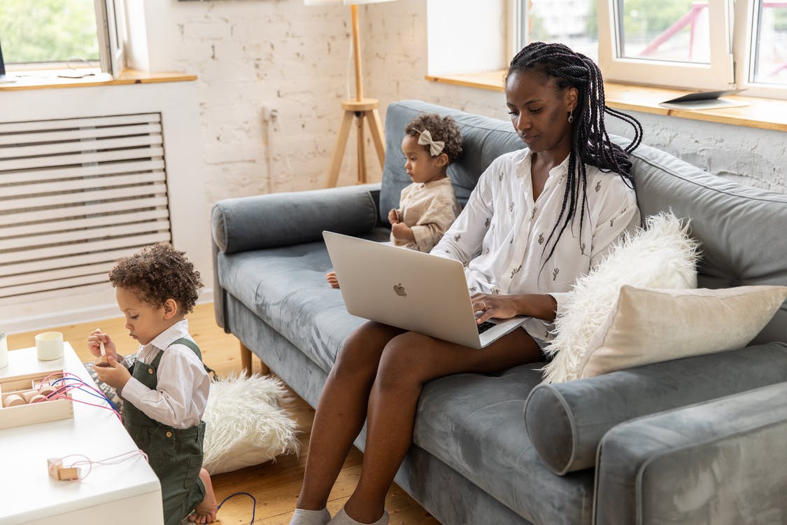 Woman in White Long Sleeve Shirt Sitting on Gray Couch Using Macbook