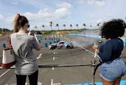 Women take selfies as a car drives past during the Red Bull Car Drift at Suncoast Hotel in Durban. 