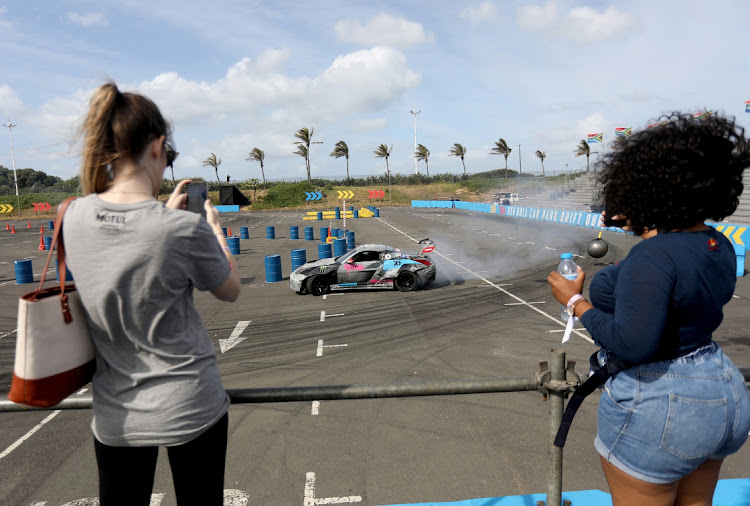 Women take selfies as a car drives past during the Red Bull Car Drift at Suncoast Hotel in Durban.