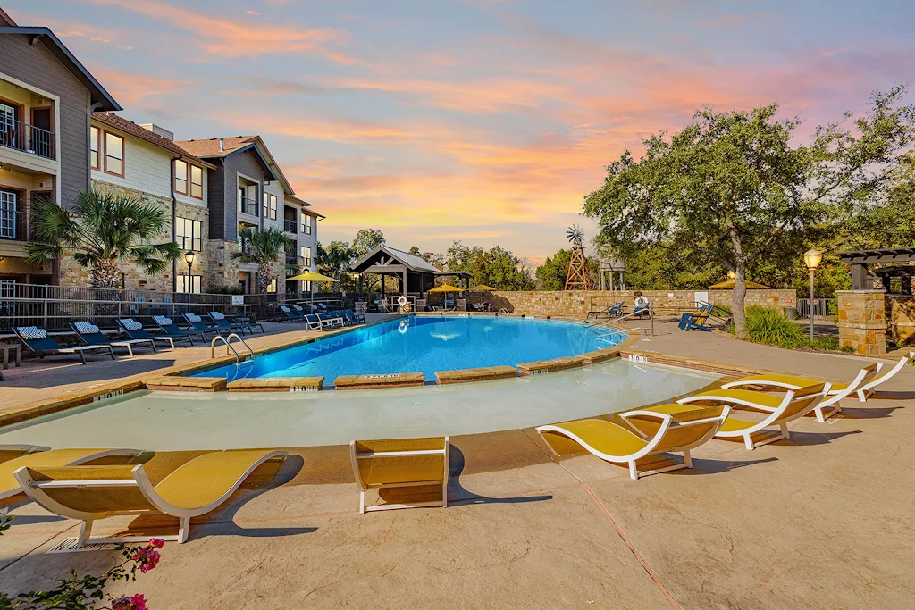 Beach access pool with yellow and blue lounge chairs, sundeck, beige apartment building in the background