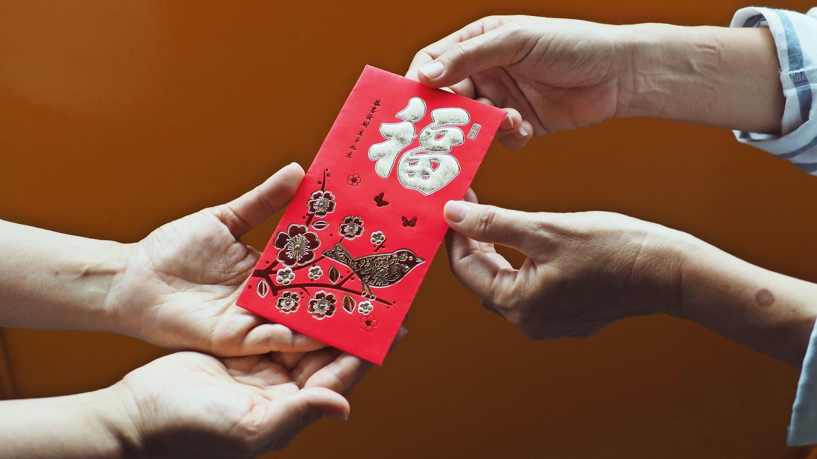 An elder hand is giving a red envelope to a child.