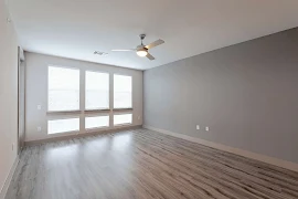 Spacious apartment living room with large windows, wood flooring, and a ceiling fan.