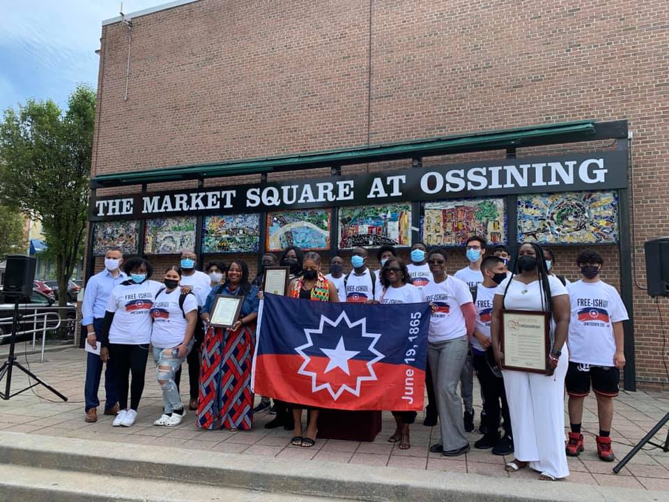 A photo of a group of community leaders and residents holding up the Juneteenth flag in Market Square, prior to its raising. 
