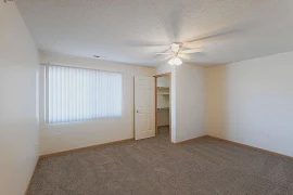 Bedroom with dark beige carpet, a window with blinds, walk-in closet, white walls and oak trim, and a ceiling fan