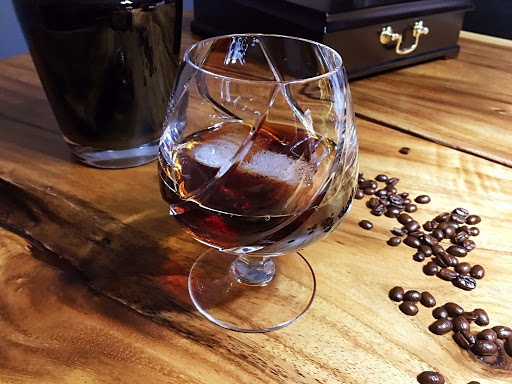 A cocktail on ice in a snifter glass with coffee beans surrounding it.