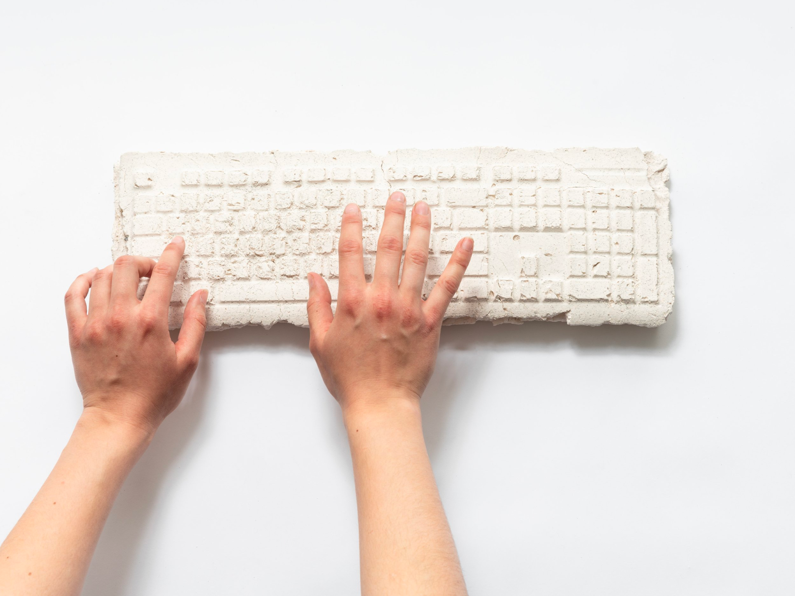 Image: Nanxi Jin, TAP TAP. A ceramic keyboard with cracks and chips in it. The keys have no detail. Two hands hover above it. Image courtesy of the artist.