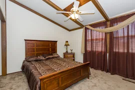 Bedroom with vaulted ceilings and beams, neutral carpet, white walls, window with blinds, brown trim