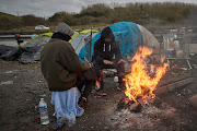 Refugees sit by a fire in the new Jungle on November 25, 2021 in Dunkirk, France. At least 27 people including five women and a young girl died on November 24 trying to cross the Channel to the UK in an inflatable dinghy in an incident which the International Organisation for Migration described as the biggest single loss of life in the Channel since it began collecting data in 2014. T