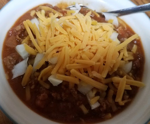 A bowl of homemade chili with chopped onions and cheese.