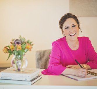 woman in a pink shirt sitting at a desk smiling