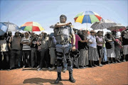 UNHAPPY:  A riot unit police officer keeps watch as Ratanda residents listen to Police Minister Nathi Mthethwa's address on service delivery following violent protests. Photo: DANIEL BORN