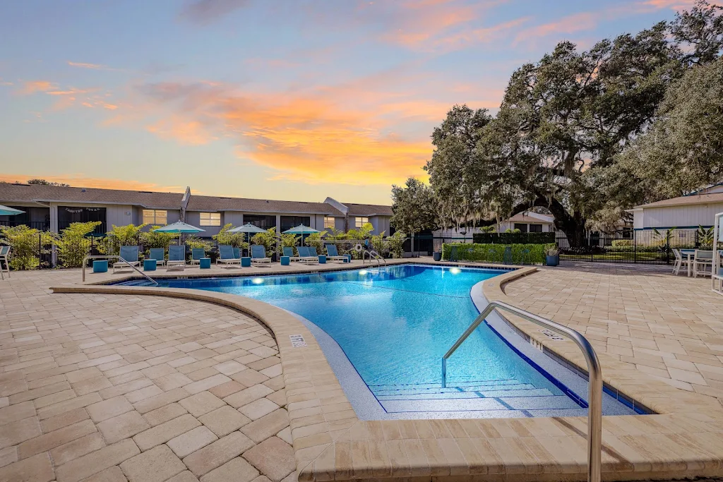 The Linx pool at dusk with 3 corner shape, surrounding brick patio has beach chairs, covered patio seating and lots of greenery.